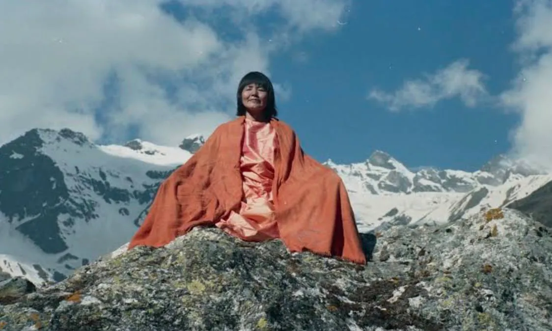 Yogmata Keiko Aikawa in Meditation auf einem Felsen im Himalaya, dahinter schneebedeckte Gipfel