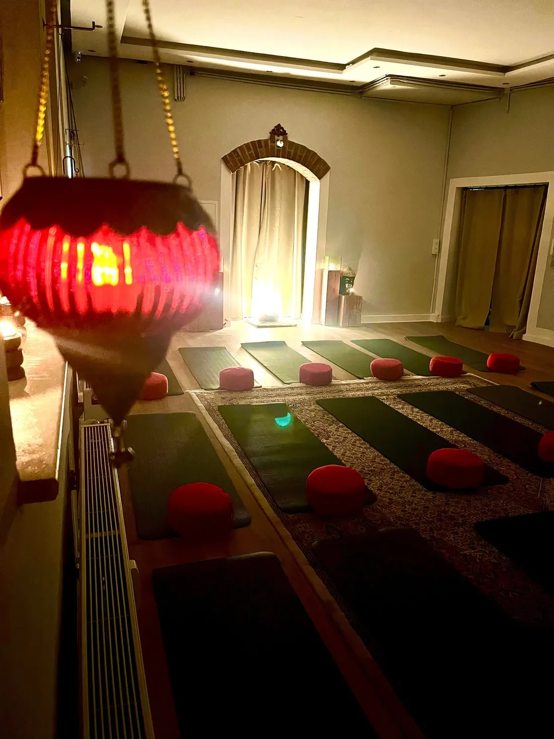 Der Meditationsraum des Shambala Instituts am Abend: Matten und rote Kissen liegen bereit, warmes Licht am Torbogen